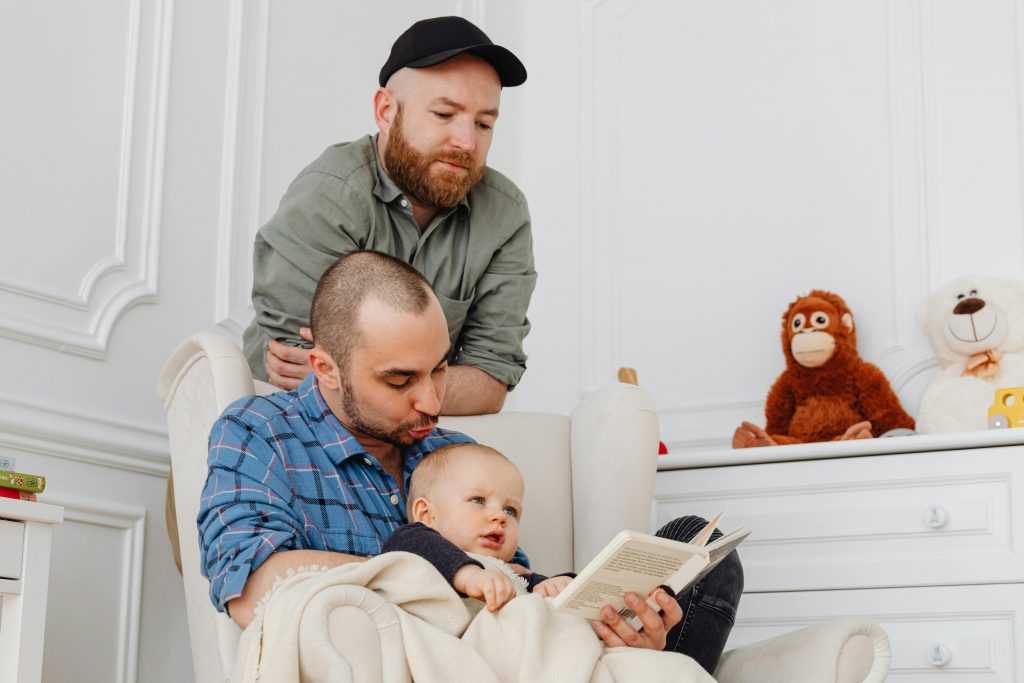 A loving moment of two dads reading to their baby in a cozy living room setting.