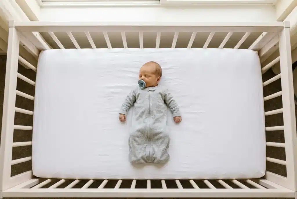 Newborn sleeping on their back in a safe, empty crib with a pacifier, following AAP safe sleep advice.