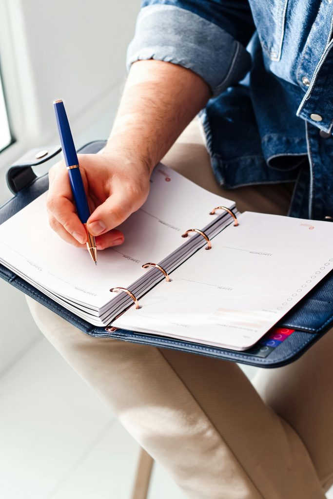 Focused image of a hand writing in a planner for goal schedule organization.