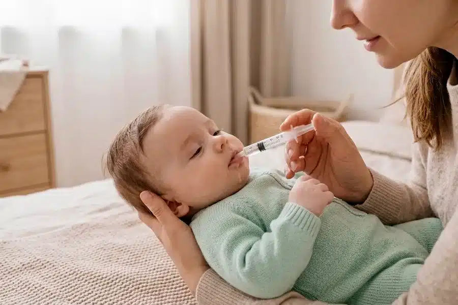Mother using oral syringe to rehydrate baby at home following baby dehydration signs